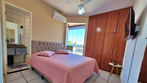 Ein Schlafzimmer mit Bett, Kleiderschrank, Deckenventilator und einem durchgegangenen Tür erkennbaren Badezimmer.