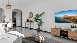 A modern living room with a large flat-screen TV, a dining area, and a minimalist design.