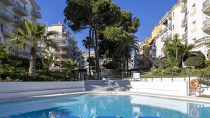 A swimming pool with blue lounge chairs, surrounded by multi-story buildings and palm trees. - Apartment in Andalucía del Mar for 4 people | ADM- 9-105 (Puerto Banús - Marbella)