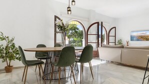 A modern dining area with a round table, green chairs, and a wooden floor. - Apartment in Andalucía del Mar for 4 people | ADM- 9-105 (Puerto Banús - Marbella)