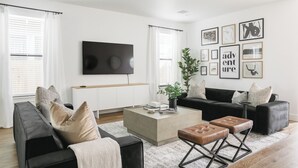 Un salon moderne avec un canapé noir, un fauteuil noir, une table basse et un téléviseur fixé au mur.