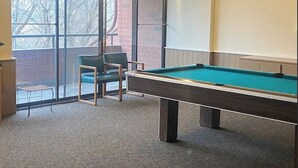 A pool table in a room with a large window, a chair, and a small table. - Charming 1 Bed Condo, Only 15 Minute Walk to Downtown (Salt Lake City)