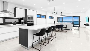 A modern kitchen with a central island, bar stools, a microwave, and a large window overlooking the sea. - Indigo Oceanfront Condo Middle Floor - Unit 2, Indigo Oceanview Terrace 2 (Sint Maarten)