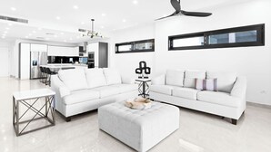 A modern living room with a white sofa, a grey ottoman, and a dining area in the background. - Indigo Oceanfront Condo Middle Floor - Unit 2, Indigo Oceanview Terrace 2 (Sint Maarten)