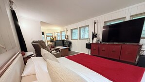 A hotel room with a bed, a desk, a chair, a television, and a red carpet.