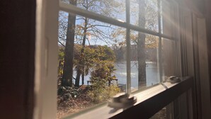 A view through a window with a clear sky, trees, and a body of water.