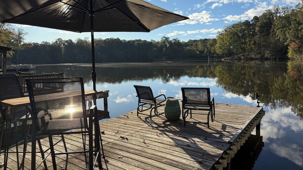 A wooden dock with chairs and an umbrella overlooking a calm lake.
