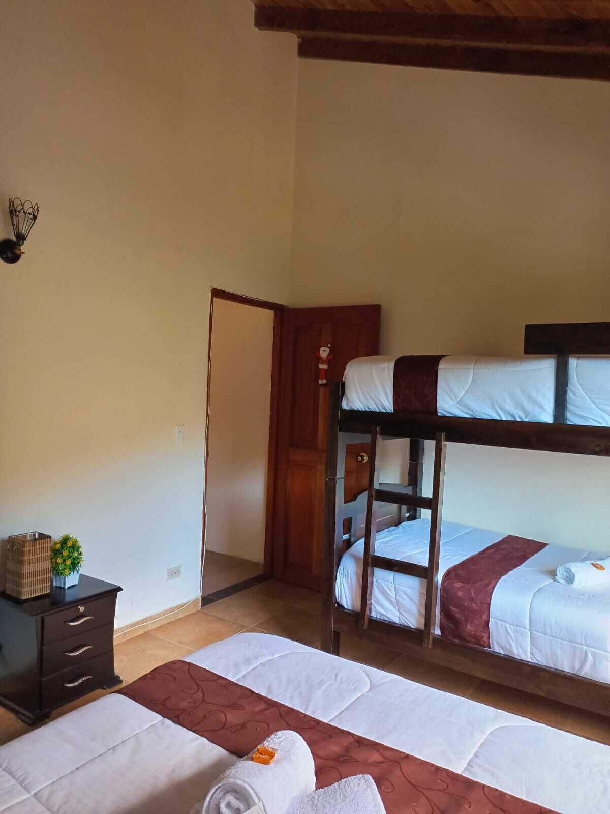 Ein Zimmer mit Etagenbetten, einem kleinen Schreibtisch mit Schubladen, einer Wandleuchte und einer Tür zu einem anderen Raum.