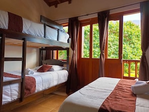 A room with bunk beds, a large window with curtains, and a view of greenery outside.