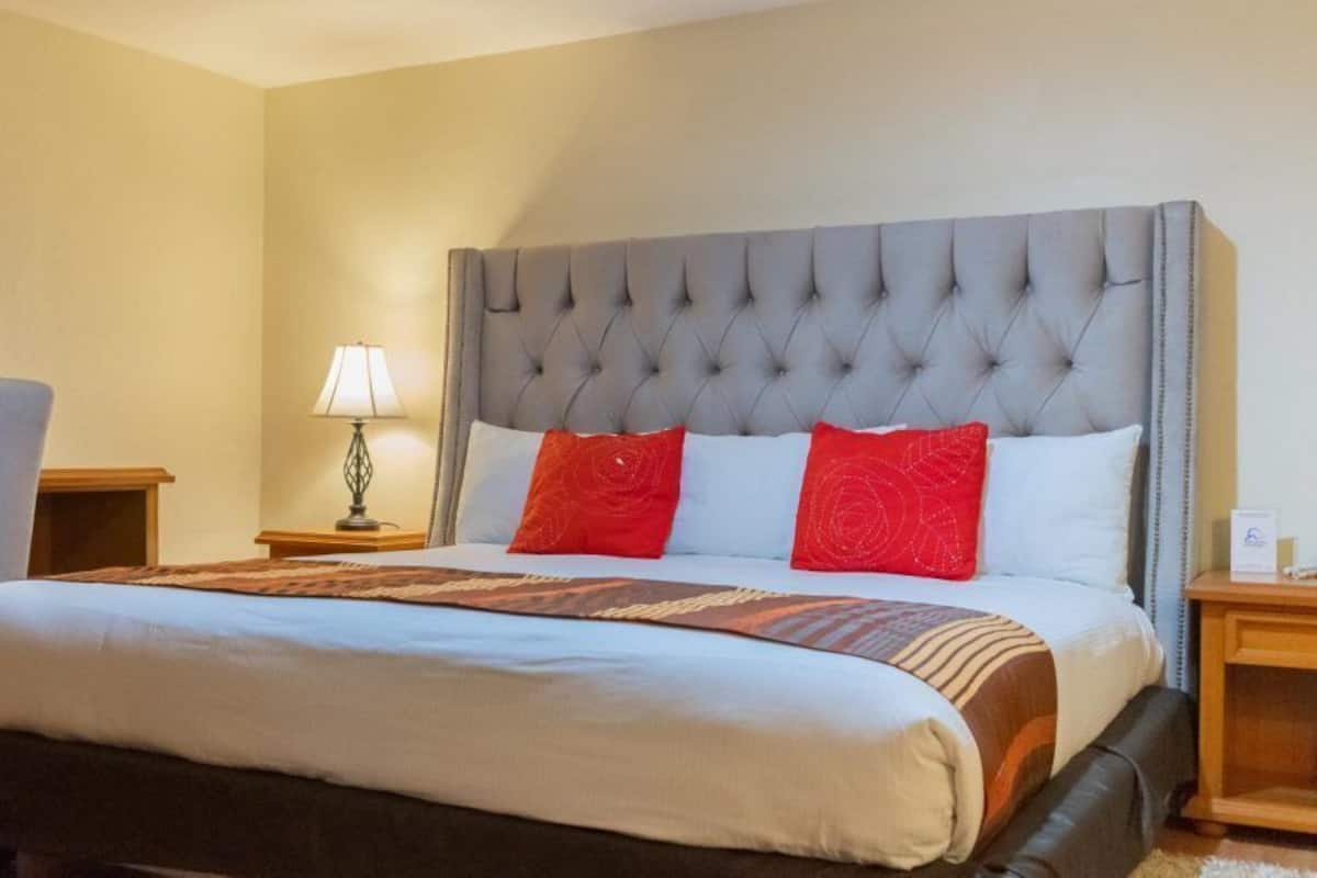 A hotel room with a large bed, a wooden nightstand, a lamp, and a chair.