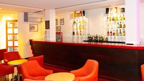 A bar area with a red counter, shelves of bottles, and orange chairs.