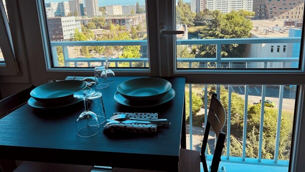 A dining table set with plates, glasses, and cutlery, overlooking a cityscape with buildings and trees.