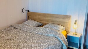 A neatly made bed with a patterned bedspread, a bedside lamp, and three framed artworks on the wall.