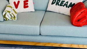 A light blue sofa with two pillows, one with "LOVE" and the other with "DREAM" embroidered in red and green respectively.