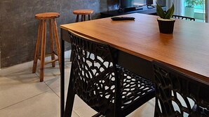 A modern kitchen with a wooden dining table, black chairs, pendant lights, and a TV. - Lindo Apartamento na Praia do Forte! (204) (Cabo Frio)