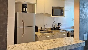 A modern kitchen with a granite countertop, two wooden stools, and pendant lighting. - Lindo Apartamento na Praia do Forte! (204) (Cabo Frio)