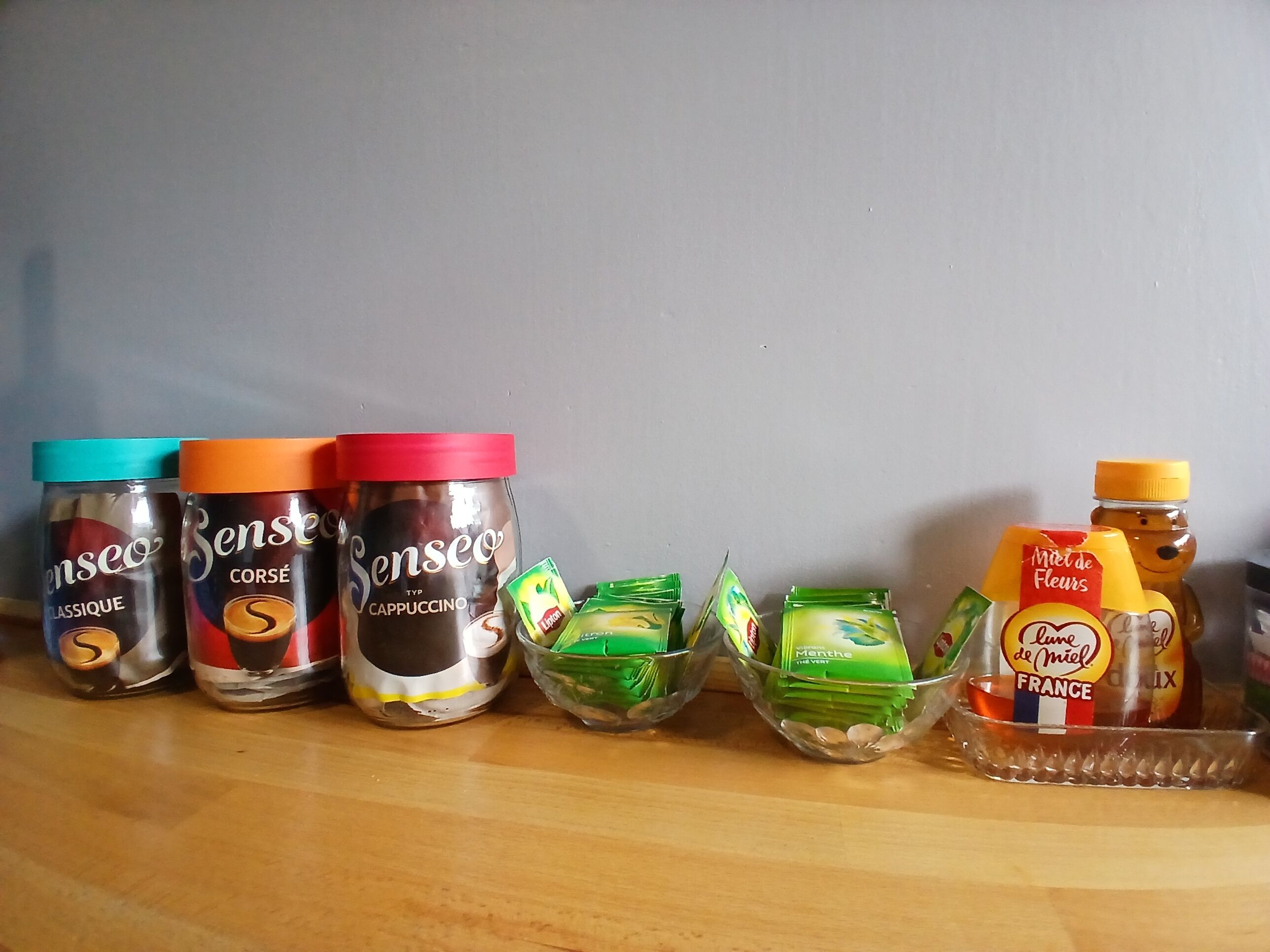 Verschiedene Lebensmittel, darunter Senseo-Kaffeegläser und Gewürze, auf einer Holztischplatte.