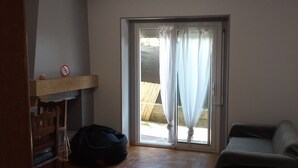 A room with a sliding glass door leading to an outdoor area, a wooden chair, a small table, and a black bag on the floor.