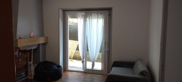 A room with a sliding glass door leading to an outdoor area, a wooden chair, a small table, and a black bag on the floor. - Pleasant 80m2 apartment in house for 6 people (Lourdes)