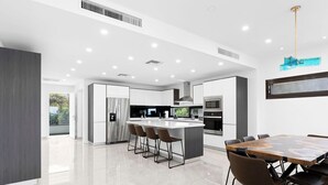 Een moderne keuken met een centraal eiland, barkrukken en een eethoek met een grote tafel en stoelen.