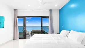 Een moderne slaapkamer met een groot bed, een plafondventilator en uitzicht op zee door een schuifdeur.