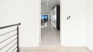 Een moderne gang met een metalen leuning, die leidt naar een kamer met een groot raam en uitzicht op de omgeving.