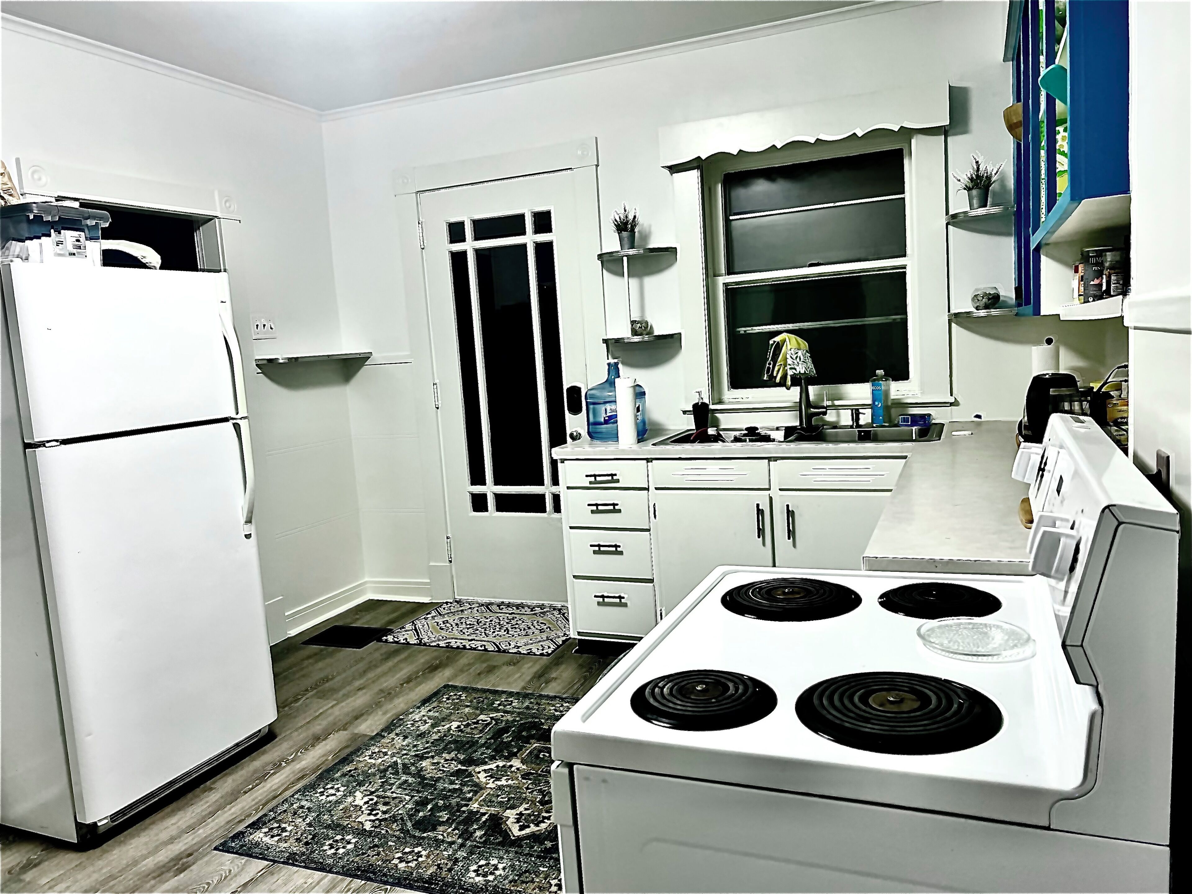 Una cocina con electrodomésticos blancos, estufa, refrigerador y ventana con vistas.