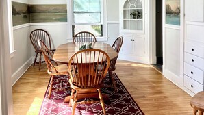 Une salle à manger avec une table et des chaises en bois, un tapis à motifs et une vue sur un paysage montagneux par la fenêtre.