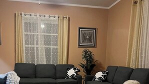 Un salon avec deux canapés sombres, une table basse en bois, des tapis à motifs et un ventilateur de plafond.