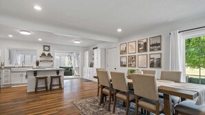 A spacious kitchen with white cabinetry, a central island with stools, and a dining area with a large table and chairs. - Charming 3-bedroom house with AC and WiFi. LAKE ACCESS King Beds! Newly Remodel (Minneapolis)