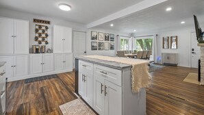 A spacious kitchen with white cabinetry, a coffee-themed wall, and a large island. - Charming 3-bedroom house with AC and WiFi. LAKE ACCESS King Beds! Newly Remodel (Minneapolis)