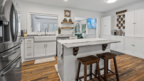 A modern kitchen with white cabinetry, a stainless steel refrigerator, a wooden island with stools, and a coffee-themed decor wall. - Charming 3-bedroom house with AC and WiFi. LAKE ACCESS King Beds! Newly Remodel (Minneapolis)