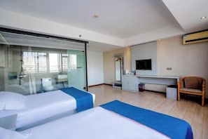 A hotel room with two beds, a desk, a chair, a TV, and a sliding glass door.