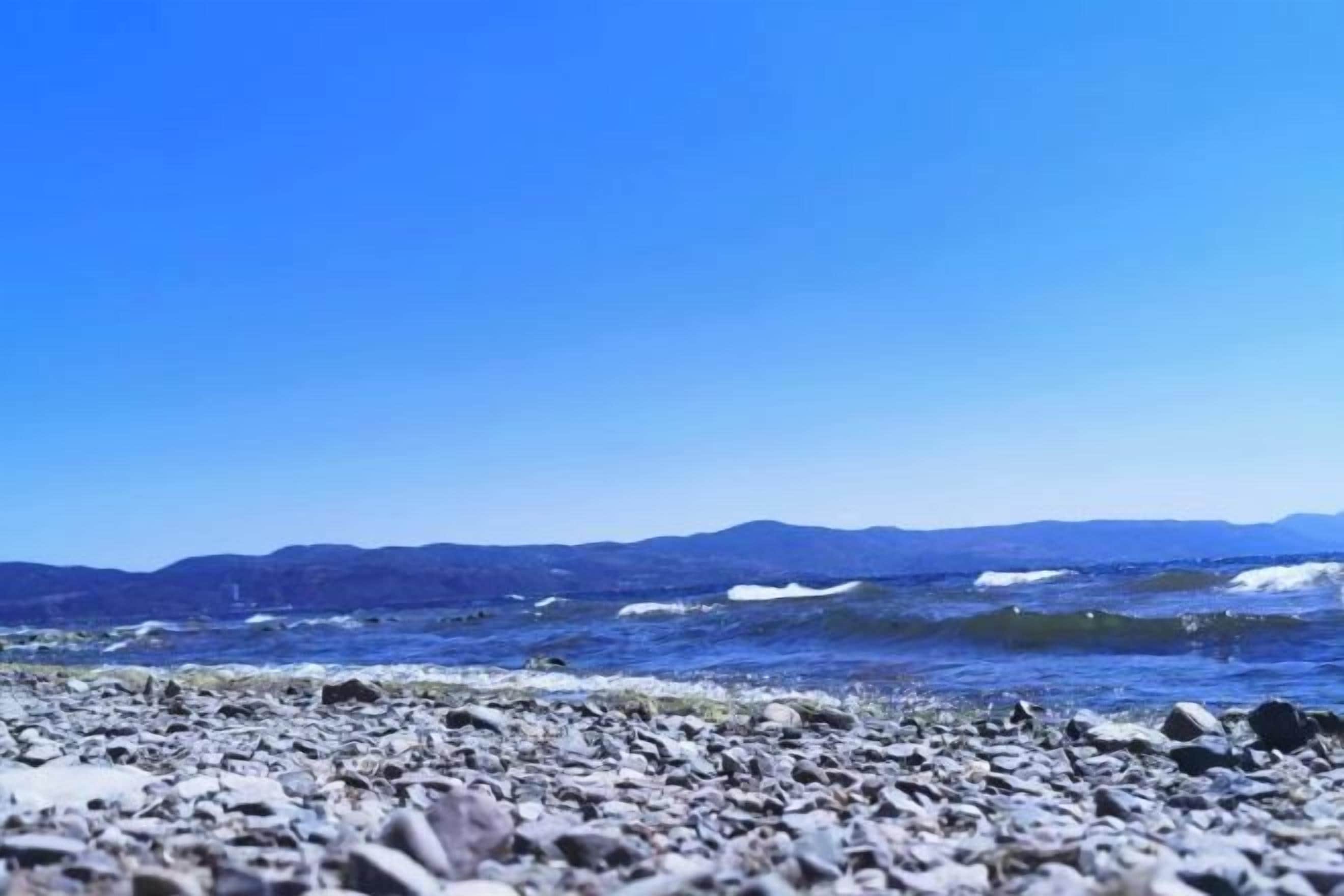 A rocky beach with waves and distant mountains.
