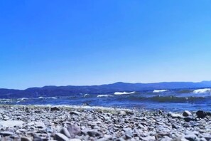 A rocky beach with waves and distant mountains.
