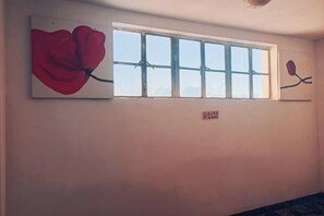 Quarto com janela, pintura de uma flor vermelha e um aviso na parede.