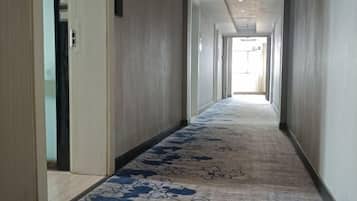 Un pasillo con alfombra estampada, puertas a ambos lados y una fuente de luz al final.
