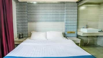 A hotel room with a bed, a nightstand, a bedside table, a built-in sink, and a red curtain.