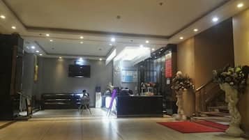 Vestíbulo de hotel con recepción, una escalera y un televisor de pantalla plana montado en la pared.