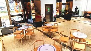 A hotel lobby with multiple seating areas, including tables and chairs, and a staircase leading to an upper level.