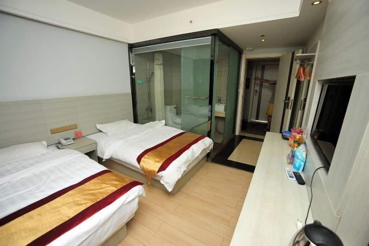 A hotel room with two beds, a desk, a shower, and a TV.
