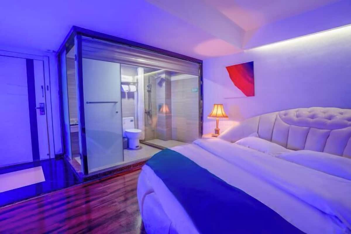 A hotel room with a bed, a glass-enclosed shower area, and a red abstract painting on the wall.