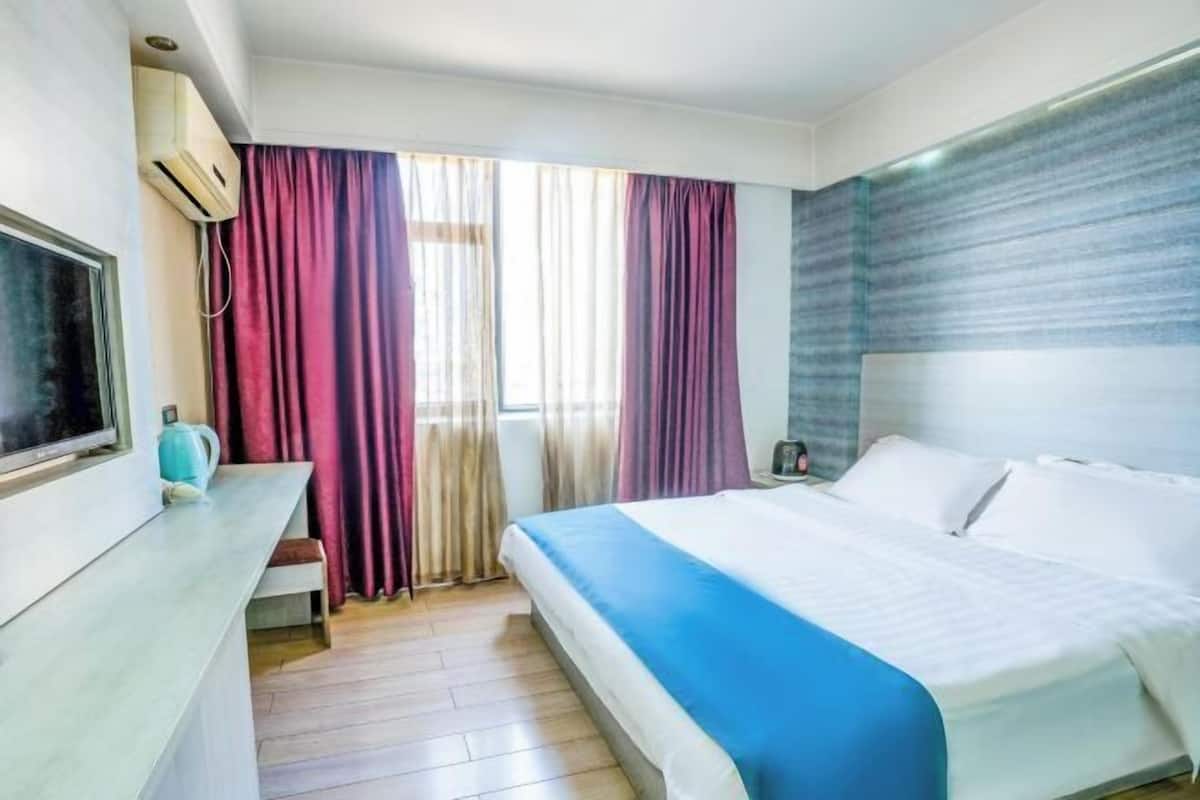 A hotel room with a bed, a TV, a desk, and curtains.