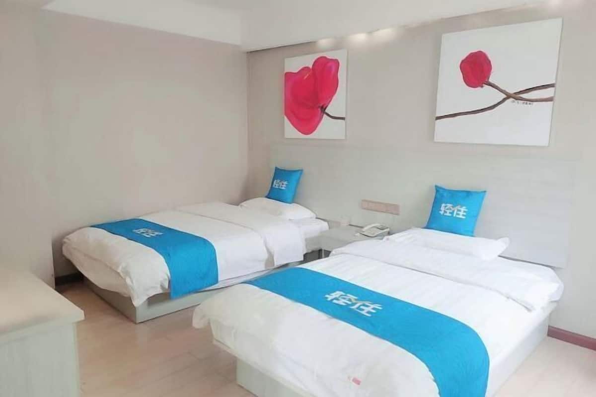 A hotel room with two beds, each with a blue and white bedspread and matching pillows. There are two paintings of red flowers on the wall.