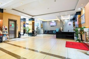 En hotellobby med en receptionsdisk, en trappa och en platt-TV på väggen.