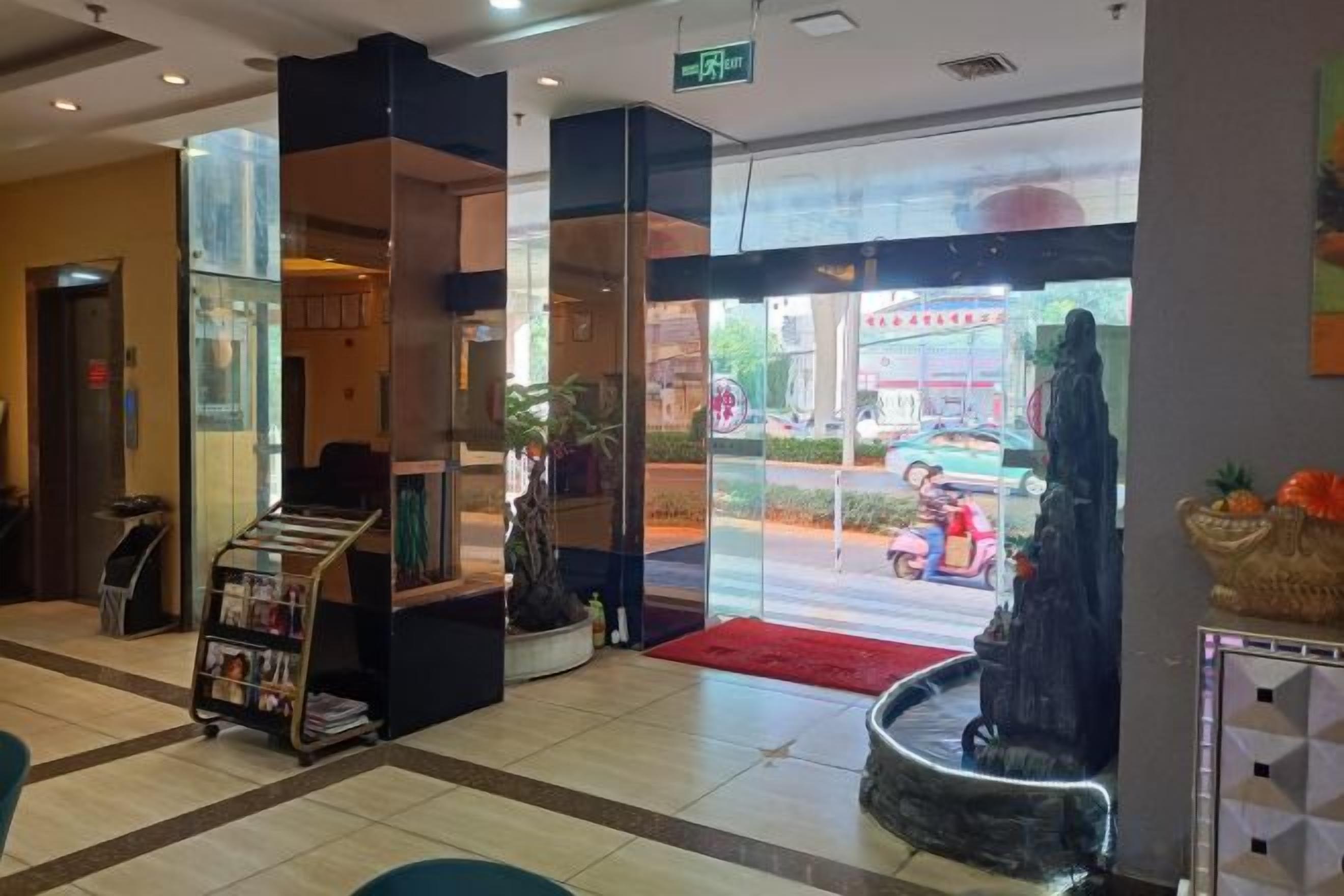 A hotel lobby with a reception desk, a magazine rack, and a red carpet leading to the entrance.