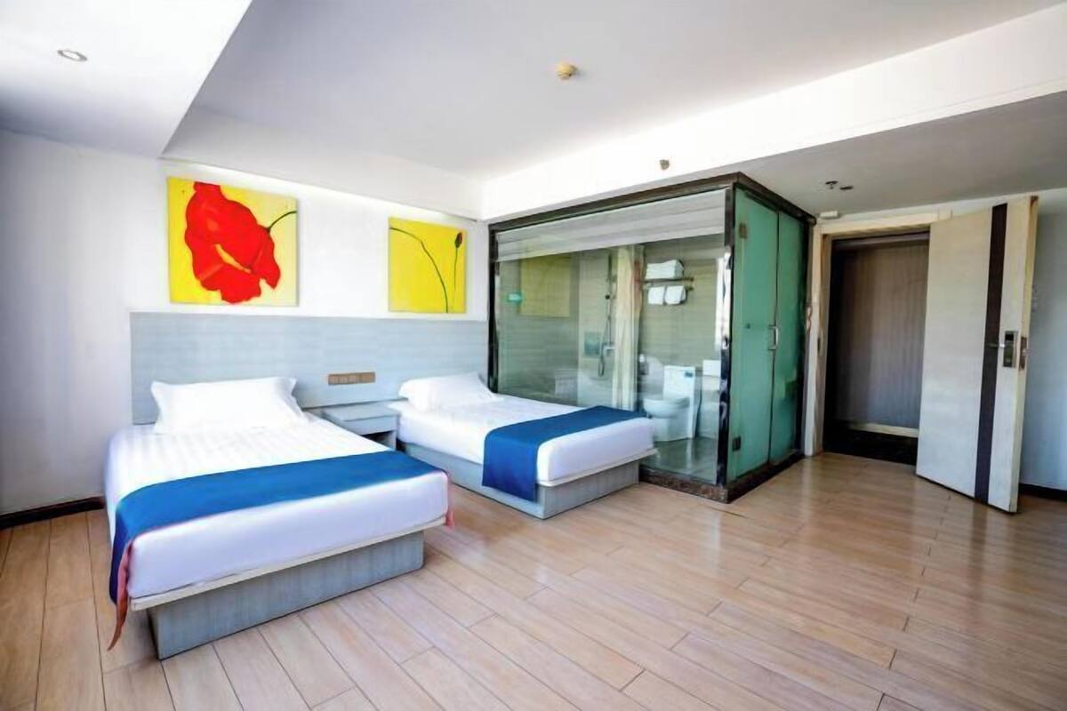 A modern hotel room with two beds, a glass shower enclosure, and a large mirror.
