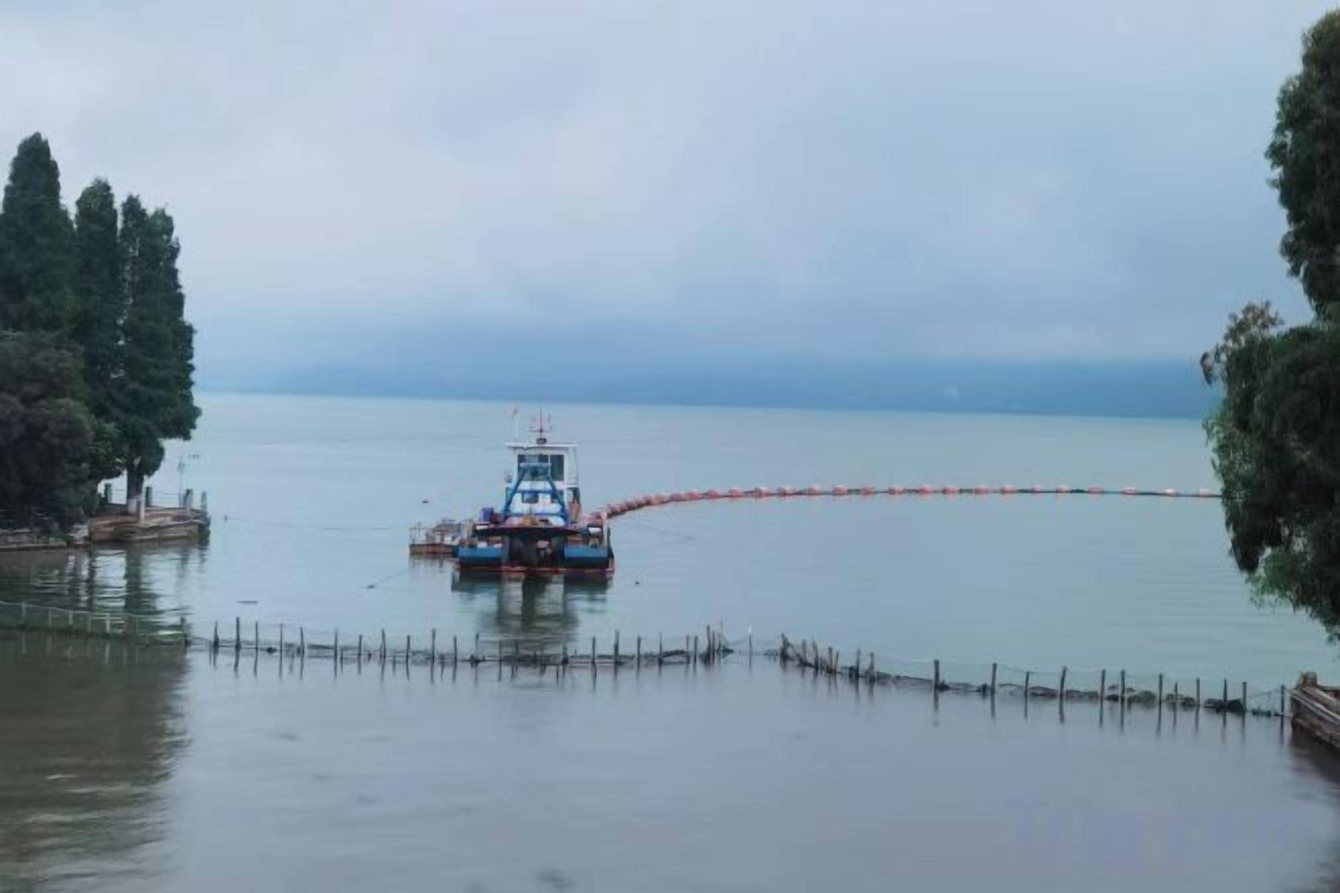 A boat on calm water with a dock on the left and a fence in the foreground.