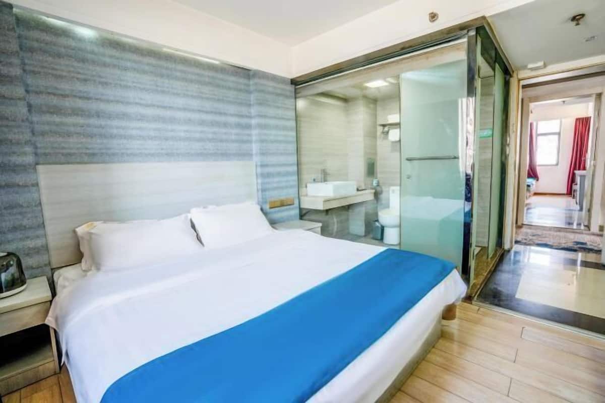 A hotel room with a large bed, a glass shower enclosure, and a visible bathroom with a sink and toilet.