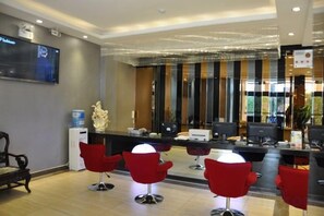 Uma área de recepção de hotel com design moderno, incluindo um balcão de atendimento, várias cadeiras e um espelho grande.
